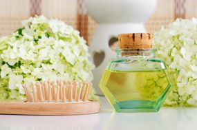 Vintage glass bottle with cosmetic oil (massage oil, tincture, infusion, extract), wooden hairbrush and white hortensia (hydrangea) flowers. Aromatherapy, homemade spa and herbal medicine concept. Copy space.