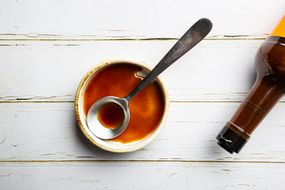 Worcestershire sauce in a bowl with spoon and bottle over white background, top view
