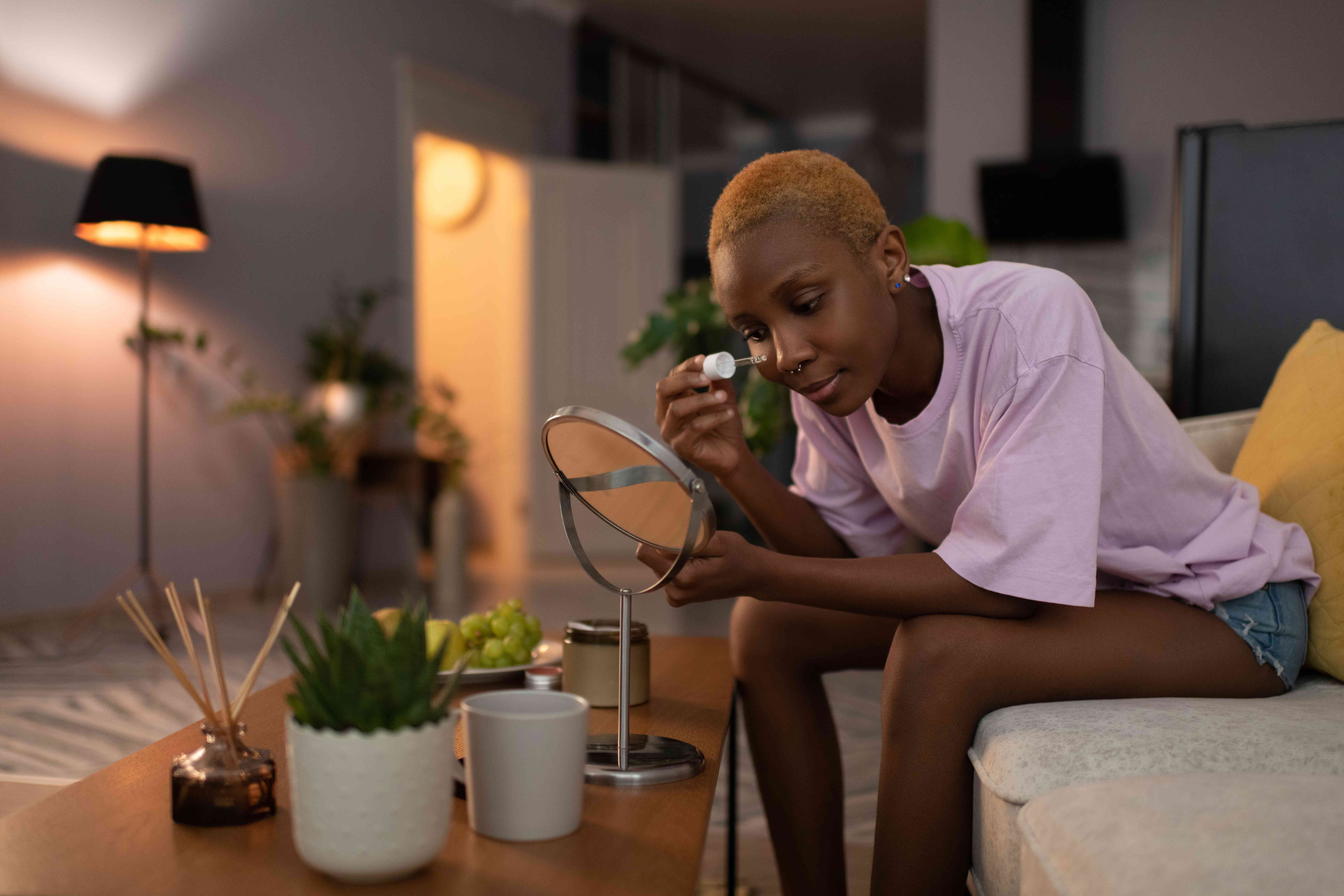 Black woman applying cosmetic product on face at home