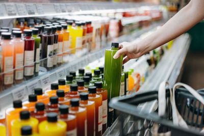 Shopper reaching for a green drink in the juice aisle“width=