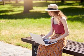 Woman sitting on park bench using her laptop with a solar charger next to her