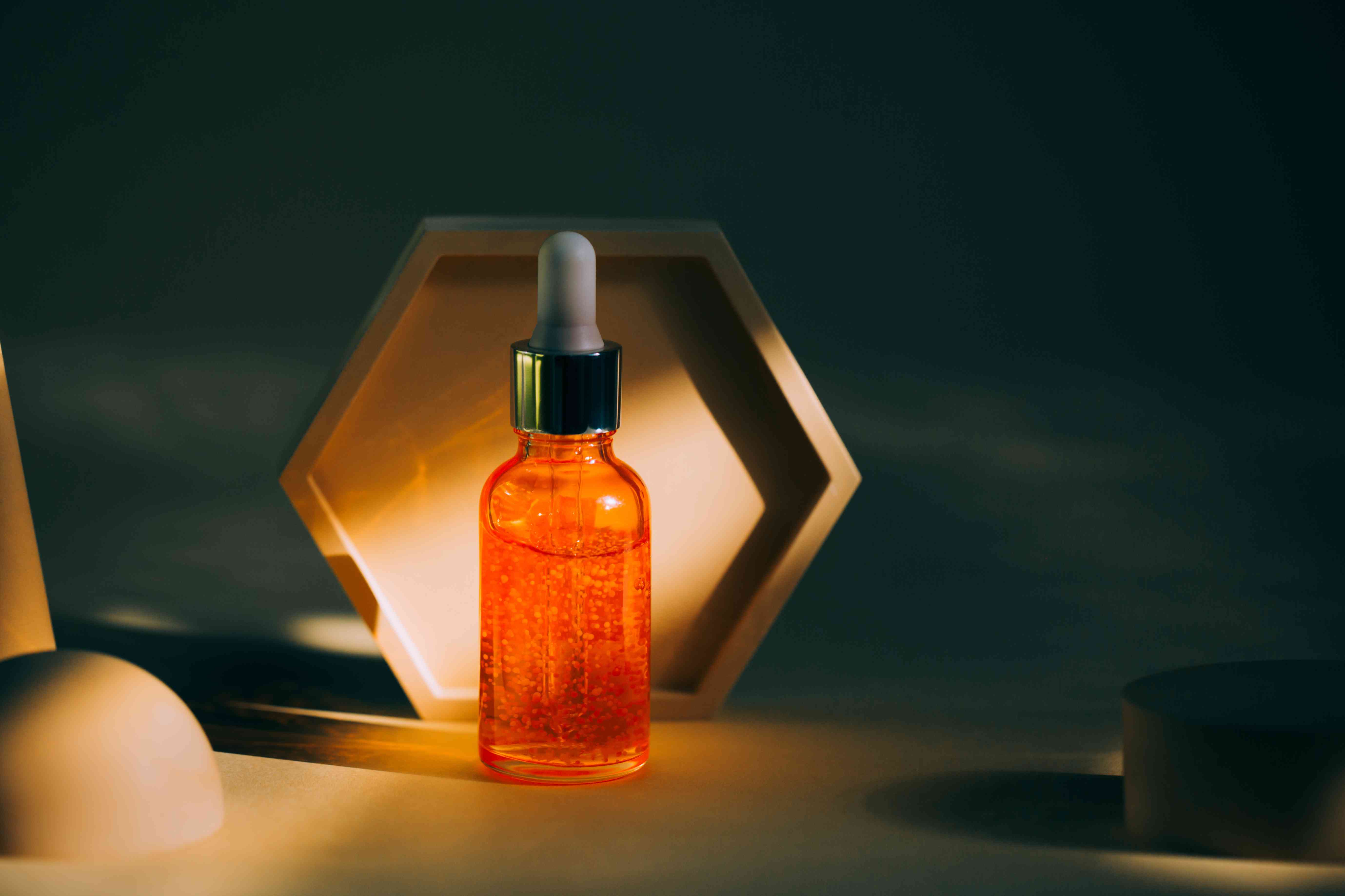 Transparent bright orange glass bottle with face serum and particles placed near set of abstract podiums on ultimate gray background. Trendy colors of the year 2021. Front view