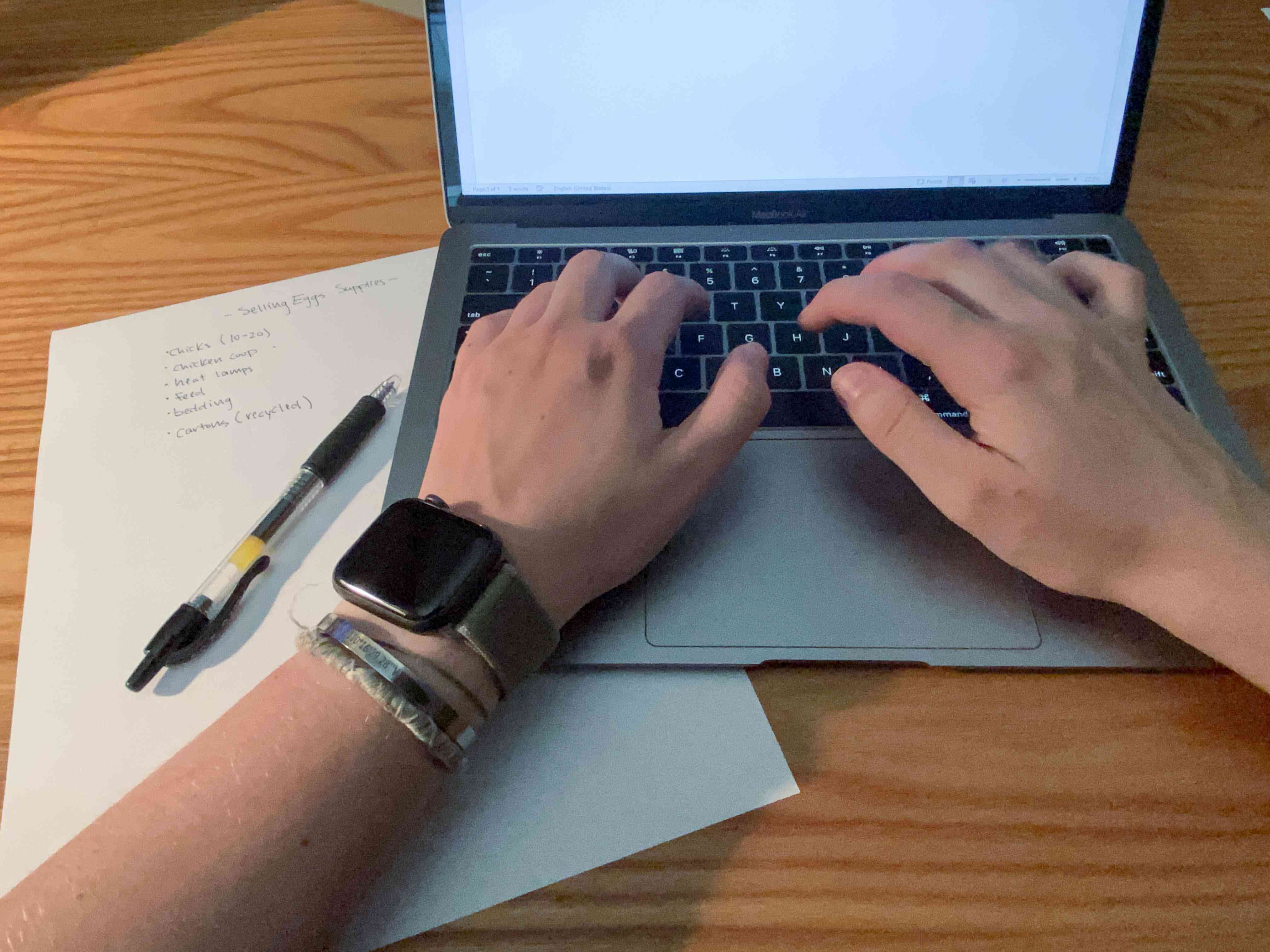 person with apple watch works on laptop with notes writing business plan