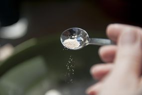 女人将酵母加入面粉制作面粉的碗中。酵母谷物掉落的关闭，被阳光照亮，从个人的角度看。