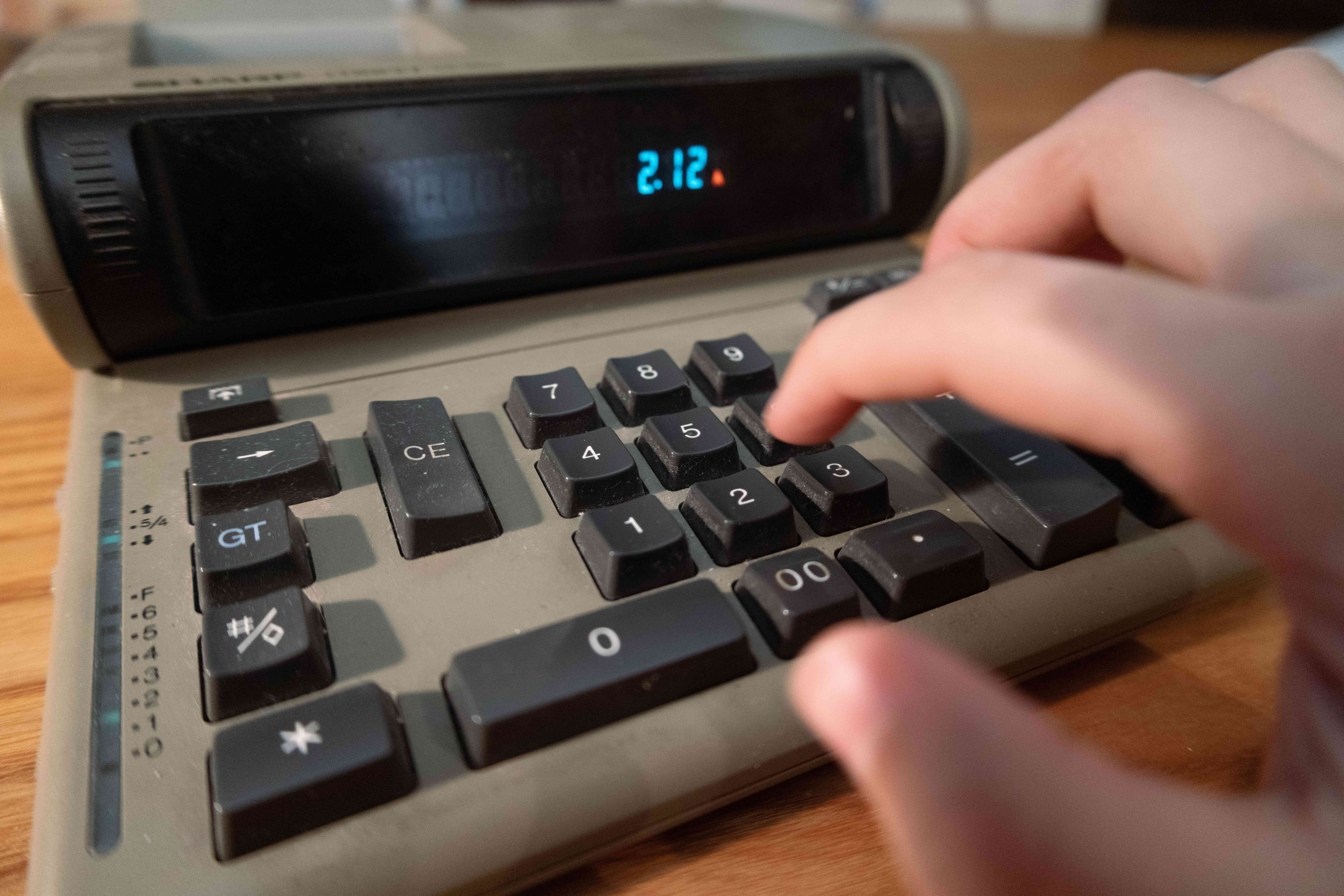 angled view of hand typing numbers into analog old school calculator