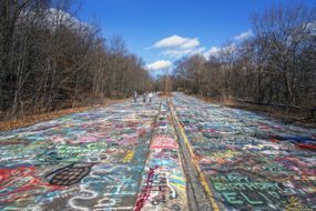 Three people walk down a road covered in graffiti